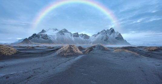 Regenbogen über einer verschneiten Bergkette.