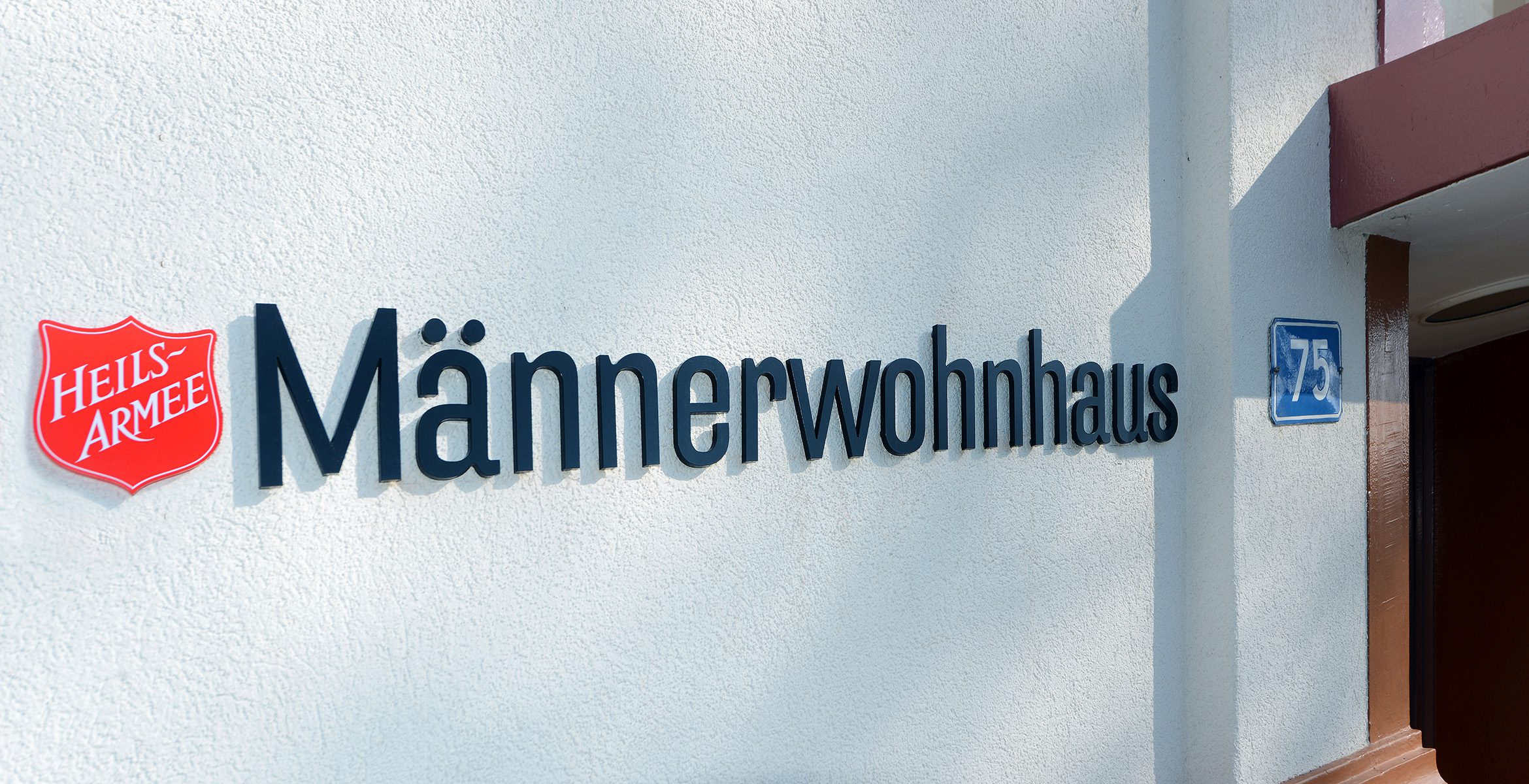 Schild «Männerwohnhaus» an der Hausfassade, © Heilsarmee Wohnen Basel