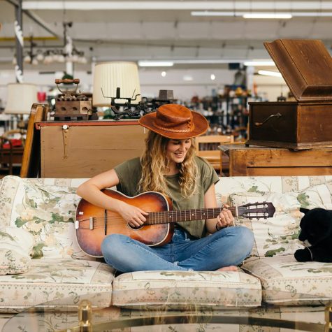 Frau mit Hut spielt Gitarre auf Sofa in einer Heilsarmee Brocki