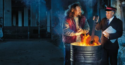 Heilsarmee Musizierender verbrennt seine Gitarre in einer Mülltonne, um damit einen Obdachlosen zu wärmen.
