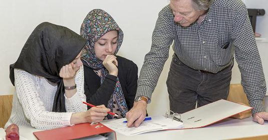 Lehrer hilft zwei Mädchen beim Deutsch lernen.