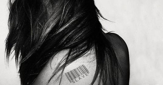 Frau, die auf ihrem Schulterblatt eine Tätowierung hat. Diese besteht aus einem Strichcode und dem Schriftzug 
