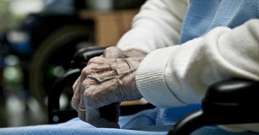 Hände einer älteren Frau im Rollstuhl.