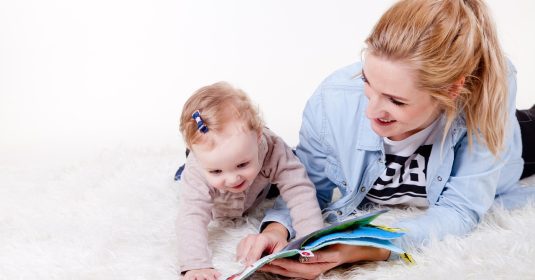 Junge Mutter entdeckt ein Knisterbuch mit Kind auf dem Teppich.